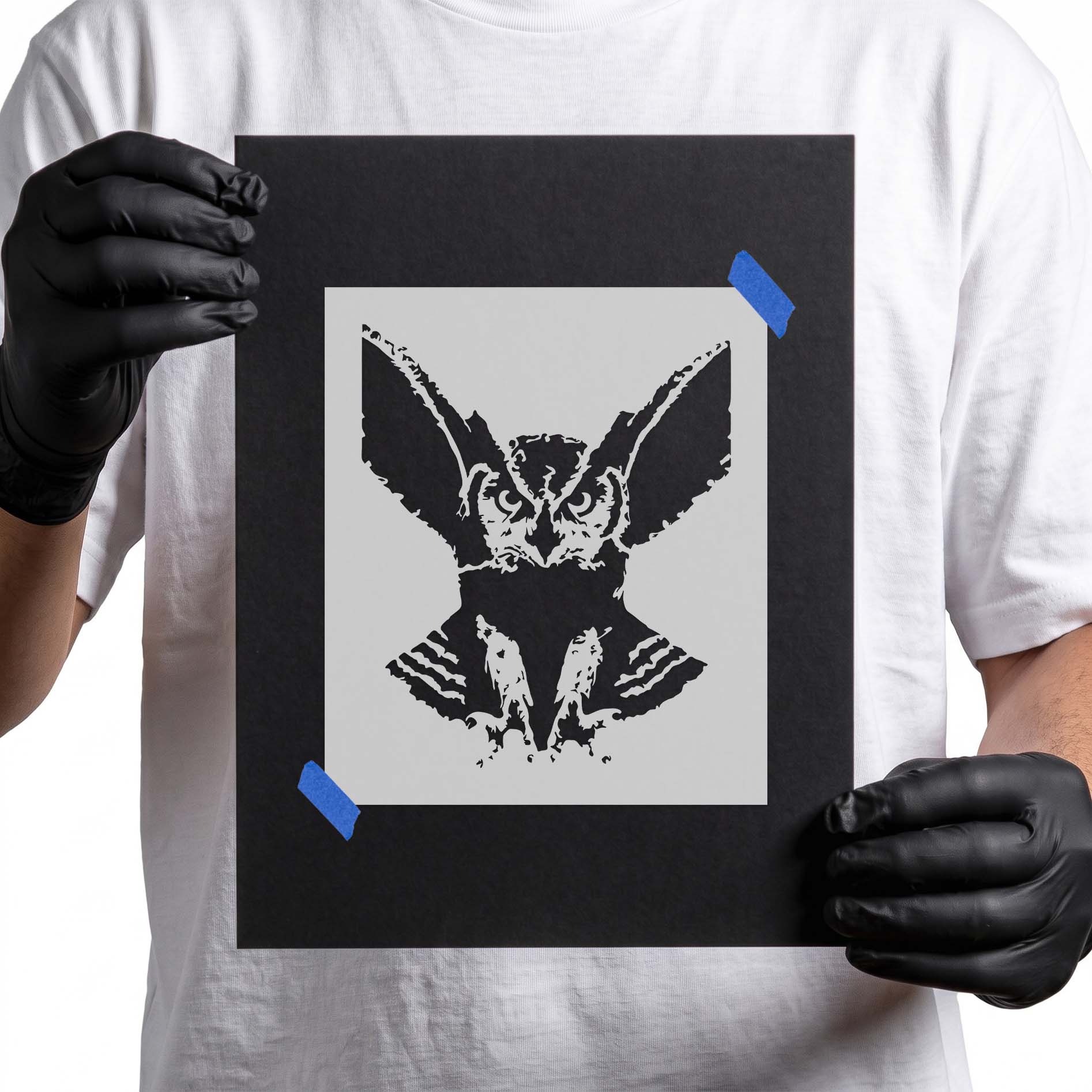 Person holding Sinister Owl Stencil taped to black cardboard
