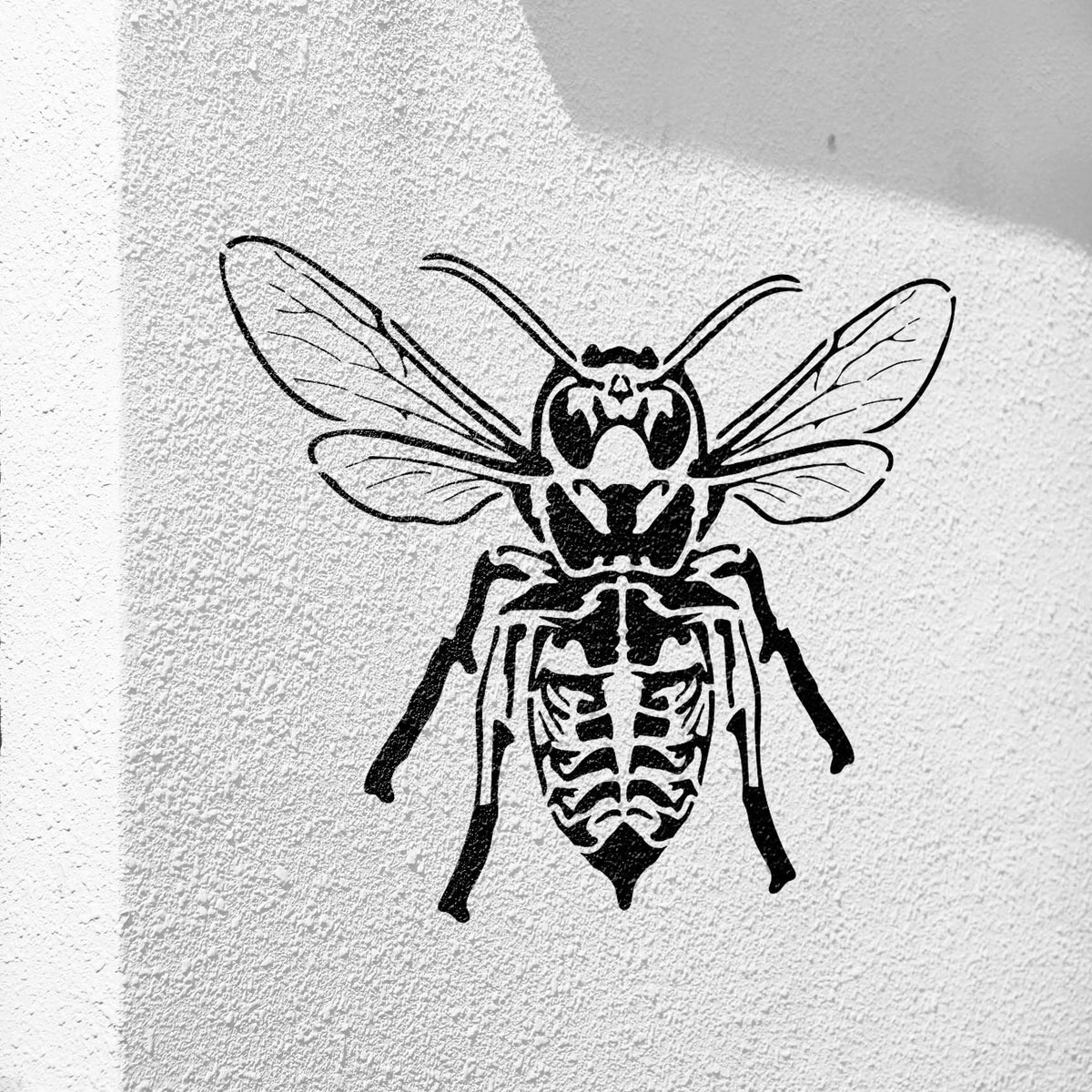 Delicate wings meet eerie skeletal details in the Skeleton Bee Stencil painted black on a textured white wall.