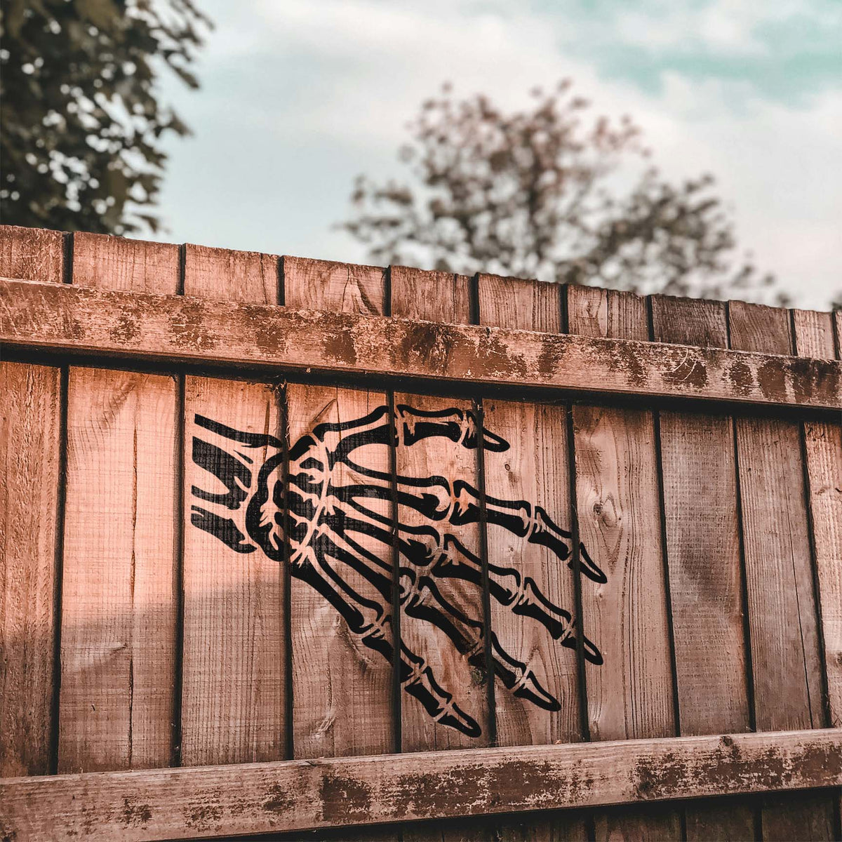 Striking Skeleton Hand Bones Stencil spans rustic wooden fence boards with extended fingers