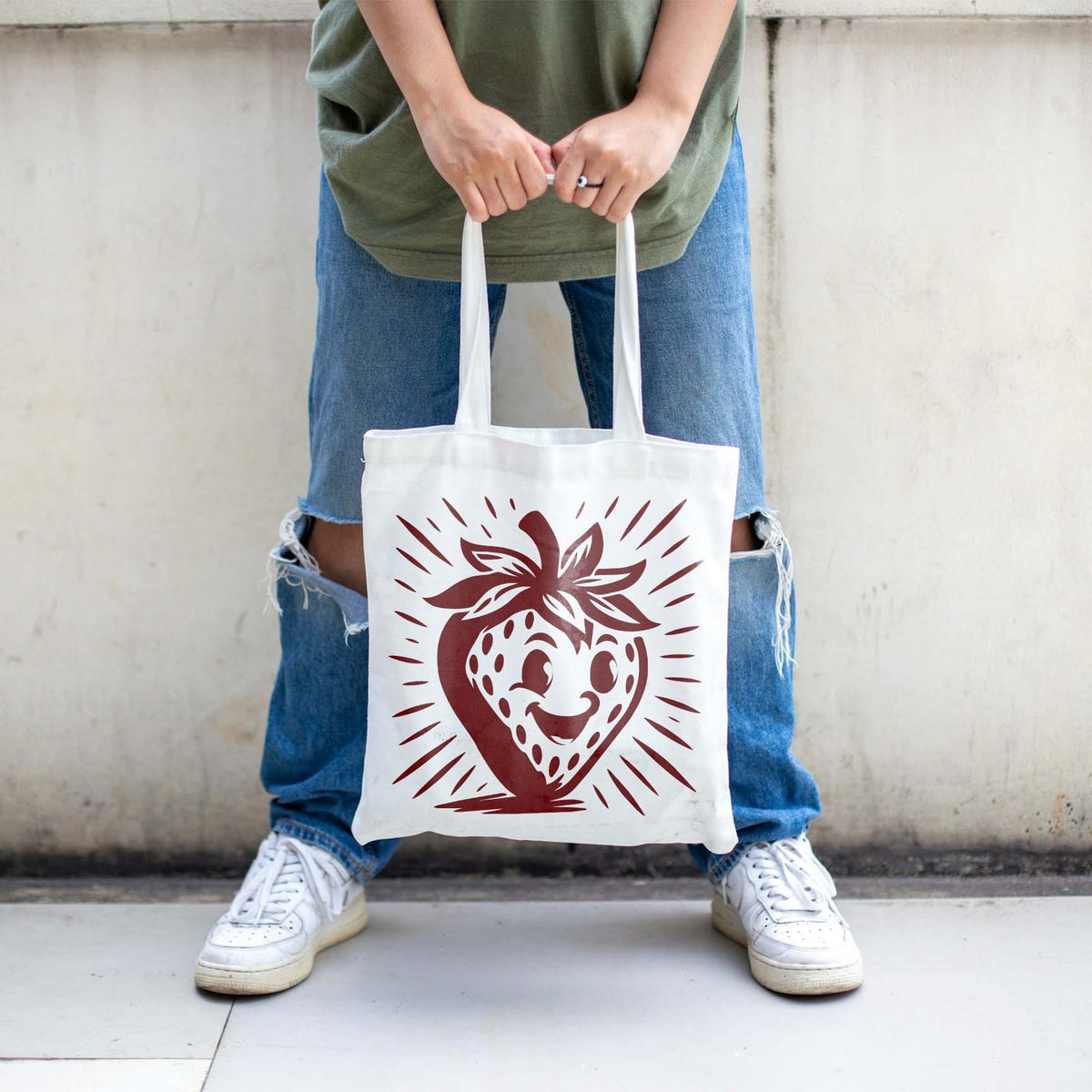 Smiling Cartoon Strawberry Stencil printed on a white tote bag held outdoors.