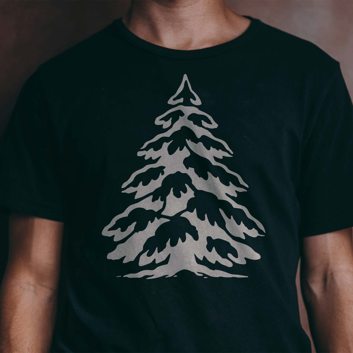 Winter-inspired Snow Covered Pine Tree stencil printed across a dark T-shirt