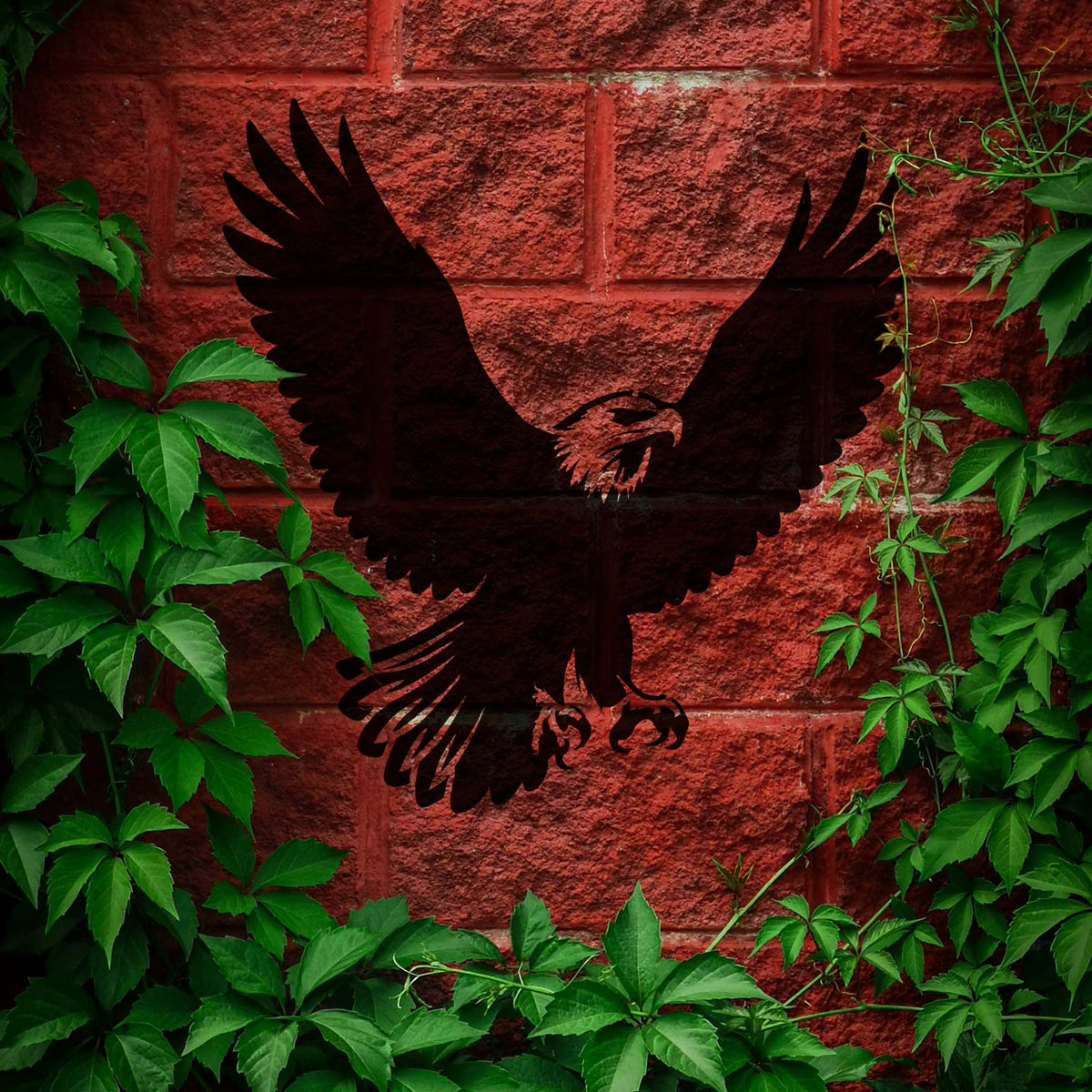 Framed by green vines, the Soaring Bald Eagle Stencil spreads its dark wings across a red brick wall.