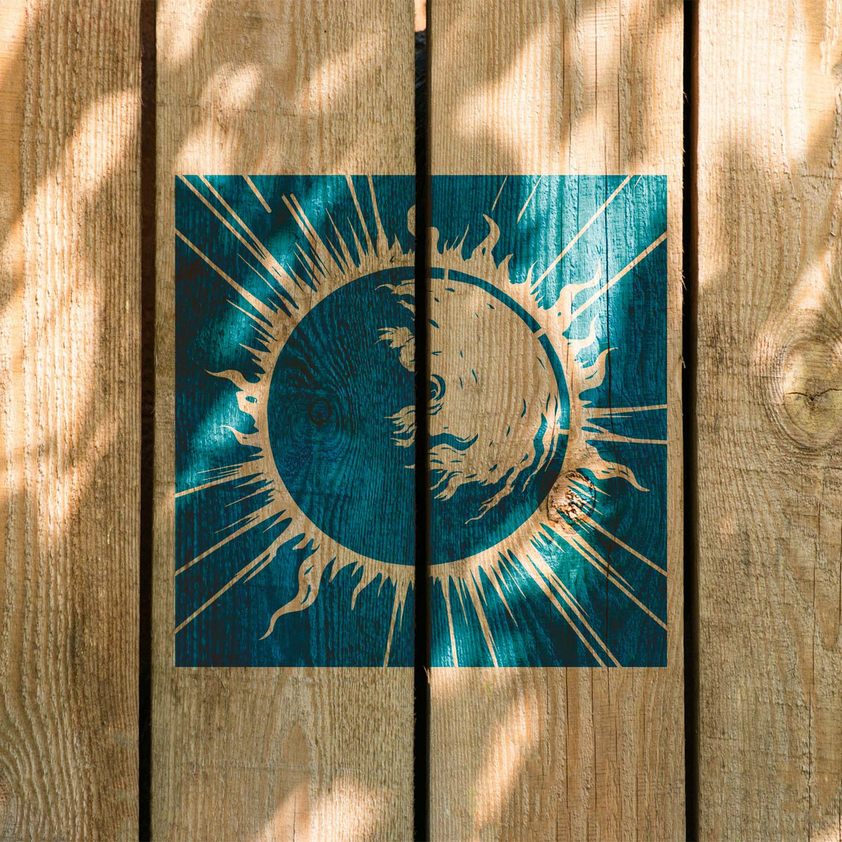 Solar Flare Eclipse Stencil stretches in vivid teal across rustic wooden planks in sunlight