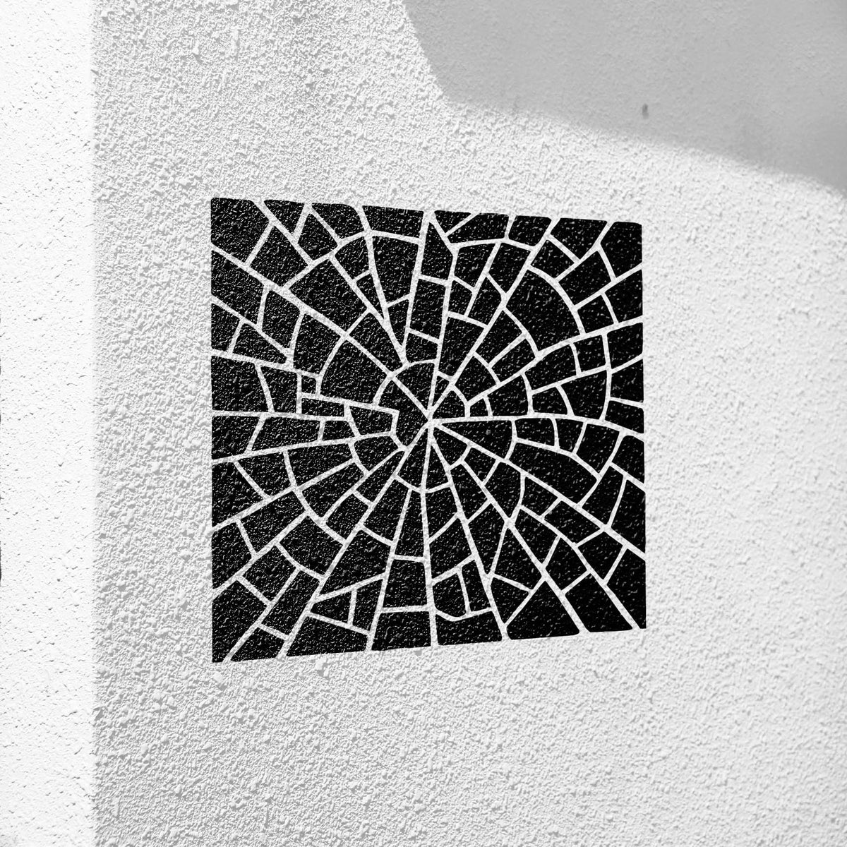Black Spiral Stone Mosaic Pattern Stencil creates a striking fragmented swirl on a white textured wall