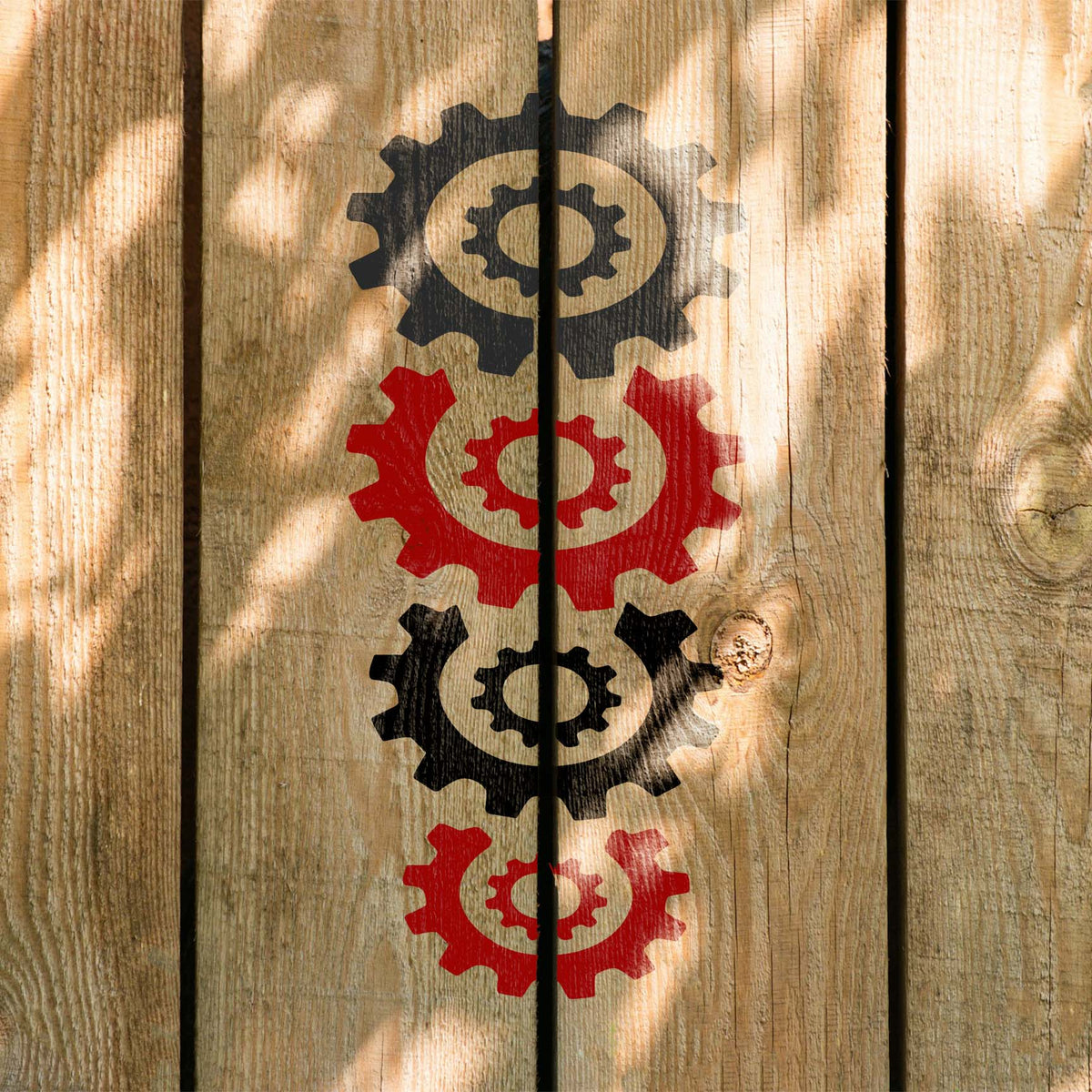 Stacked Gears stencil with alternating black and red cogwheels arranged vertically on wooden boards