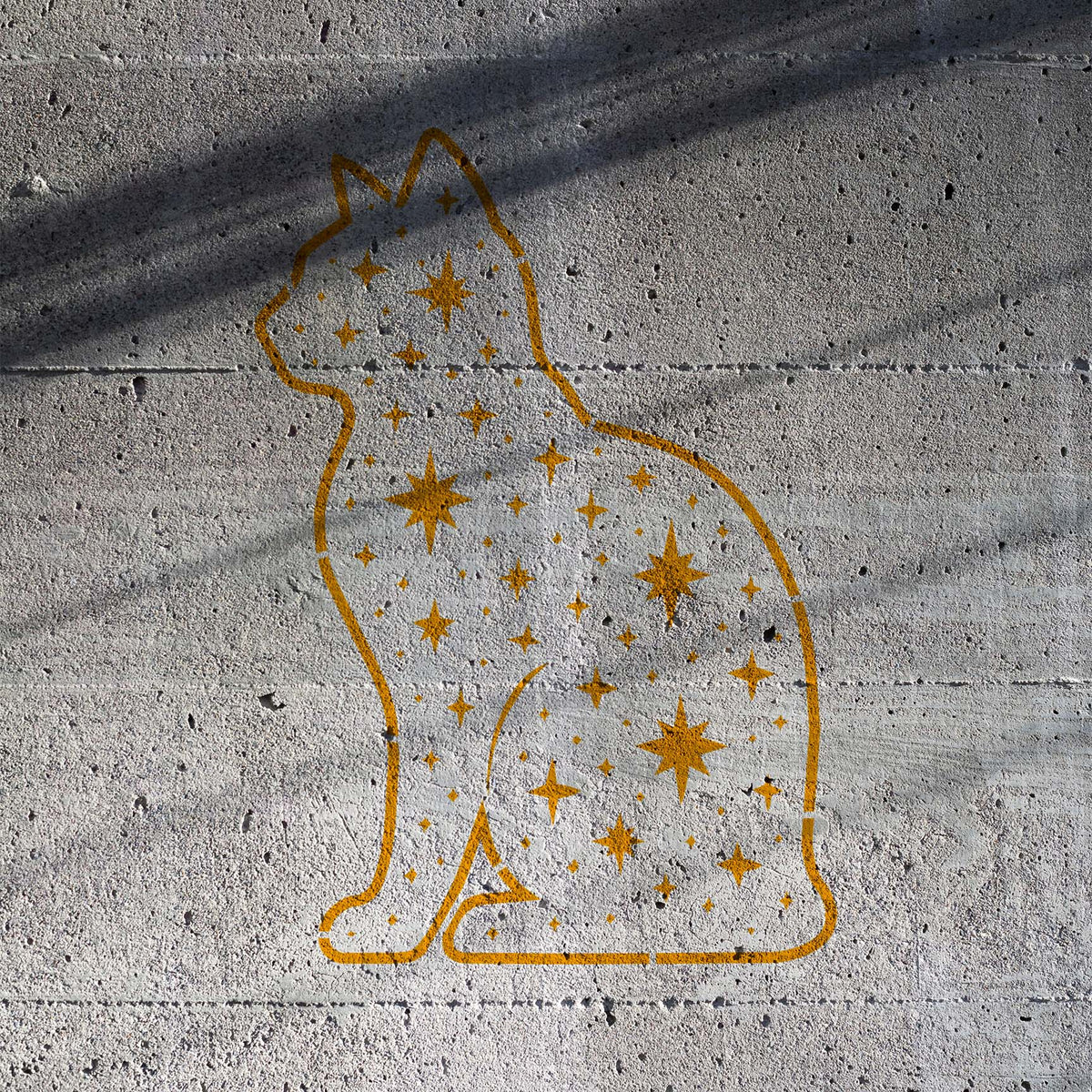 Starry Cat Silhouette Stencil glows in gold with scattered stars across a raw concrete wall