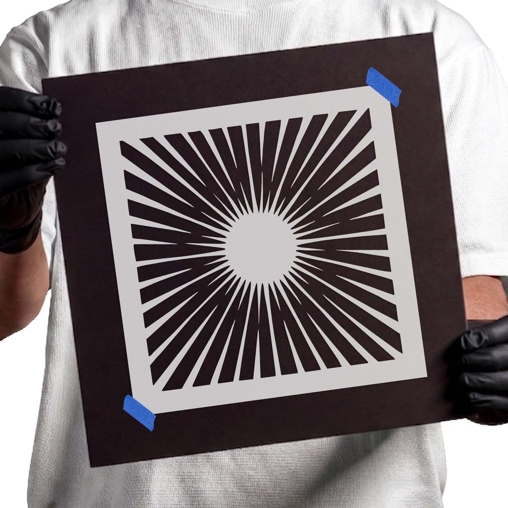 Person holding Radiant Sunburst Stencil taped to black cardboard