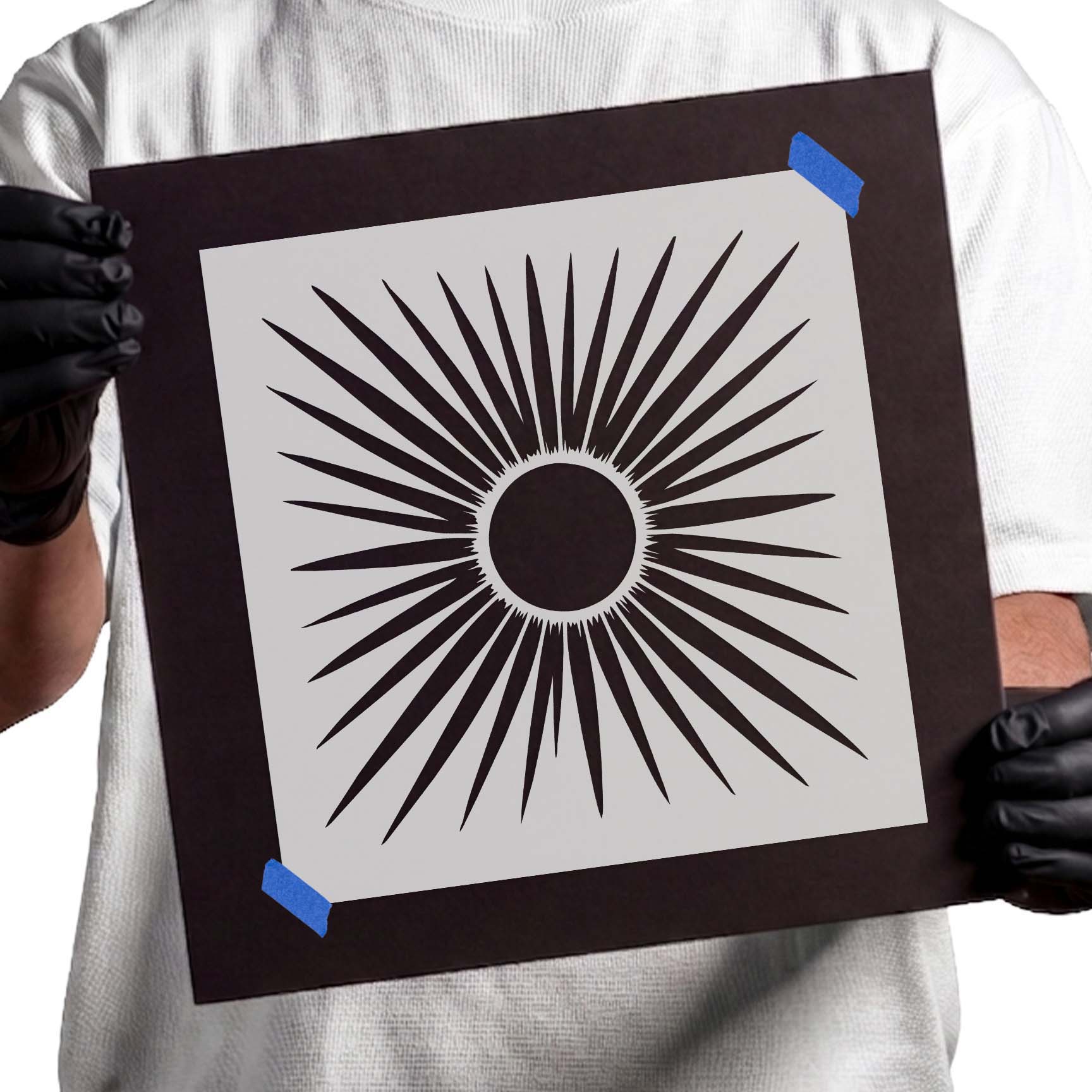 Gloved hands holding Classic Sunburst Stencil taped to cardboard