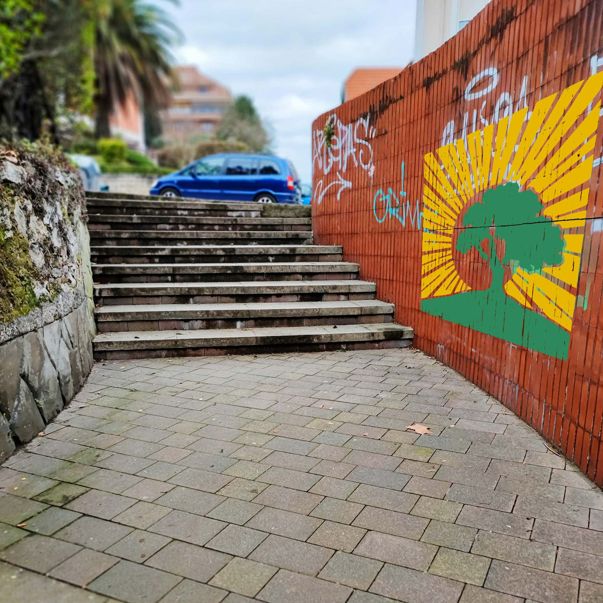 Along an urban brick wall, the Sunrise Tree Silhouette Stencil adds a bold green tree and golden rays