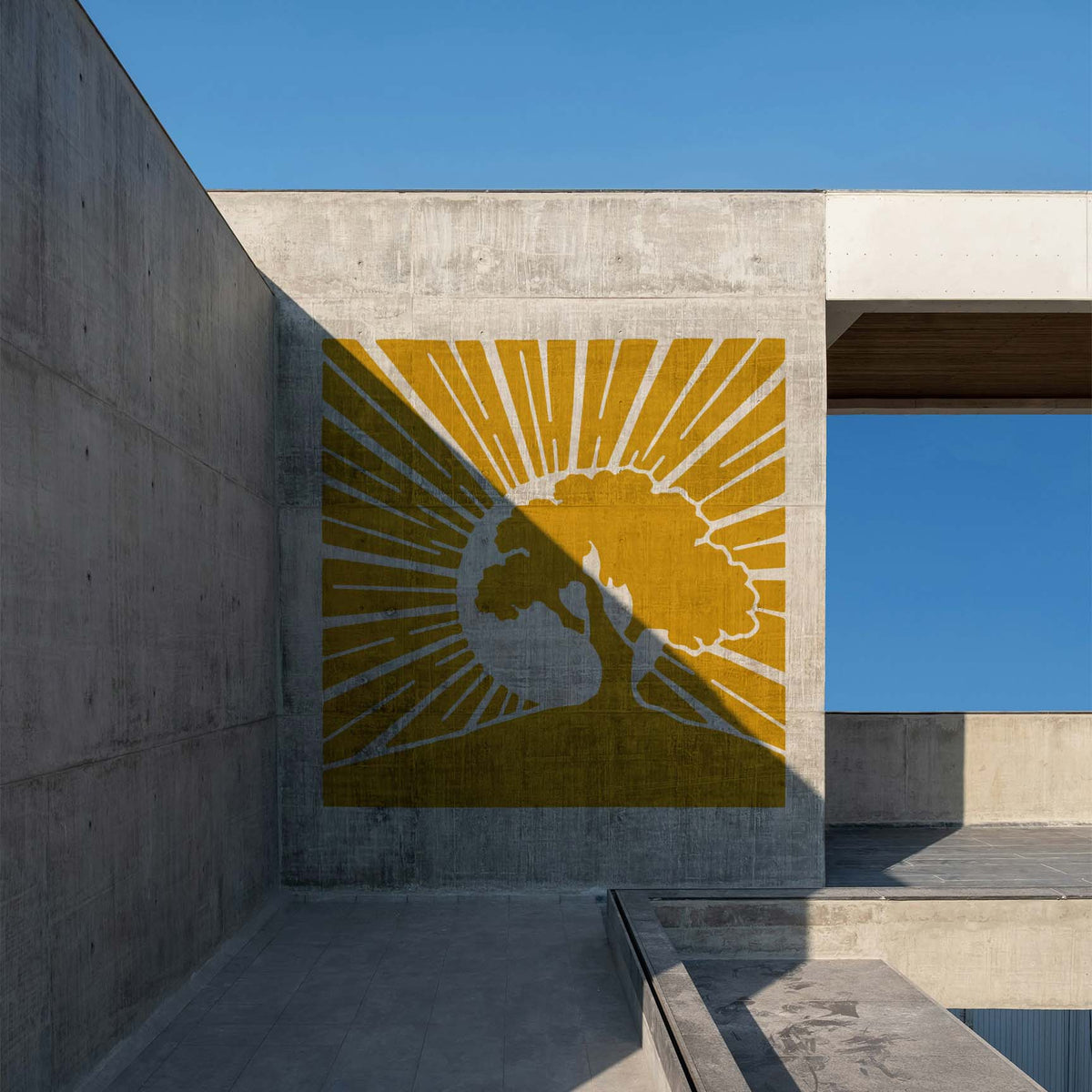 A modern concrete wall showcases the Sunrise Tree Silhouette Stencil in golden yellow beneath the blue sky.
