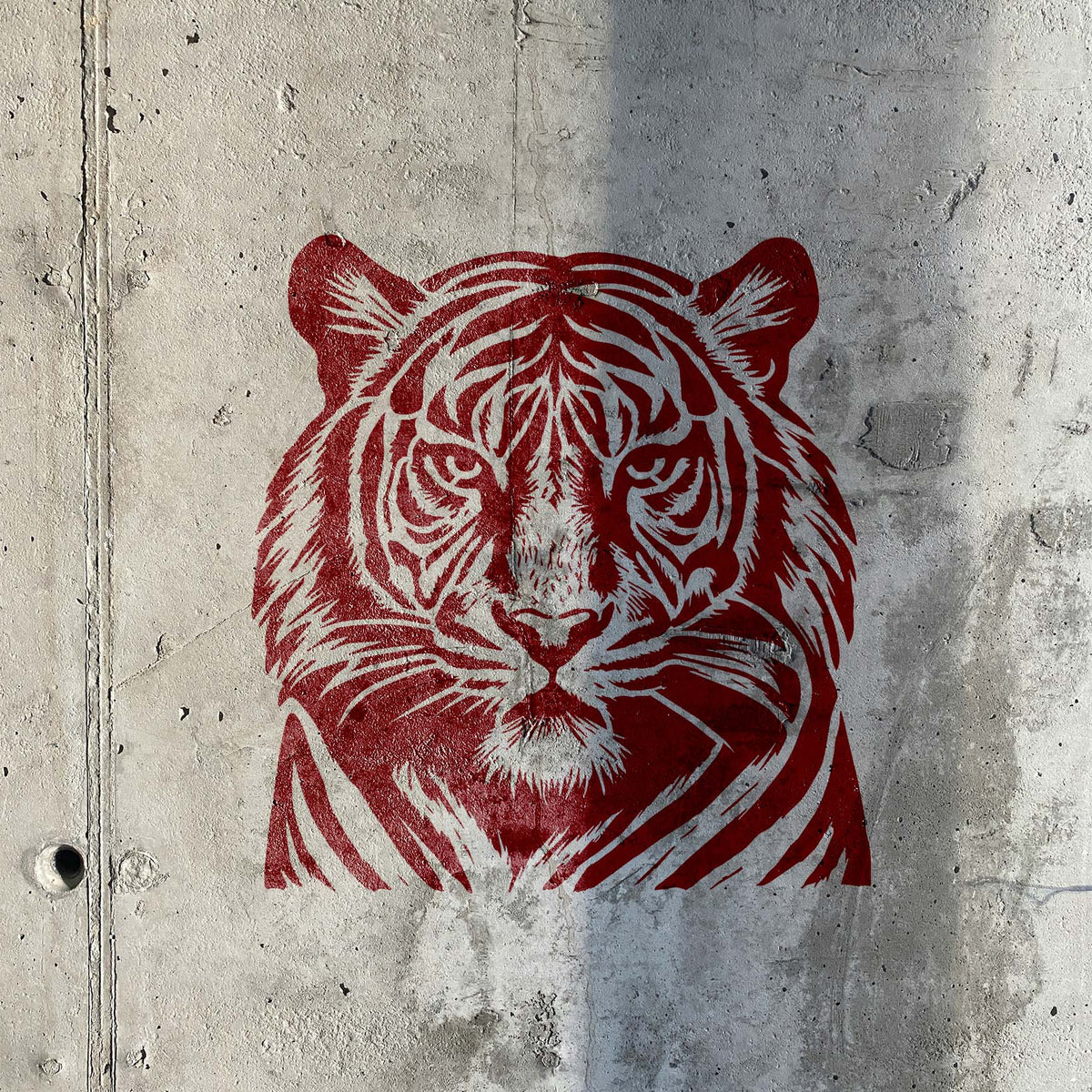 Detailed Tiger Face Wildlife Stencil in red on a textured concrete wall.