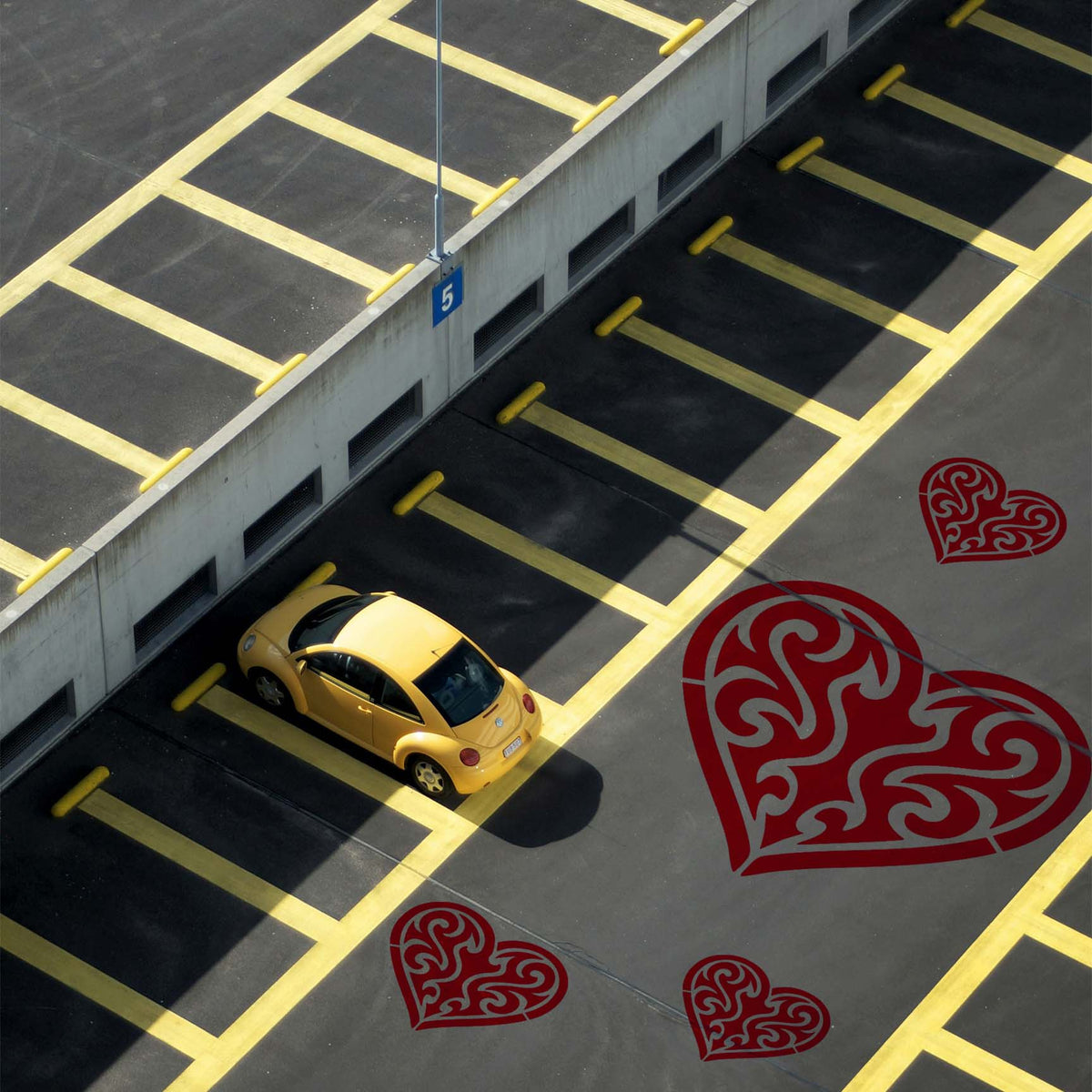Oversized Tribal Heart Stencil motifs decorate asphalt beside yellow parking space lines