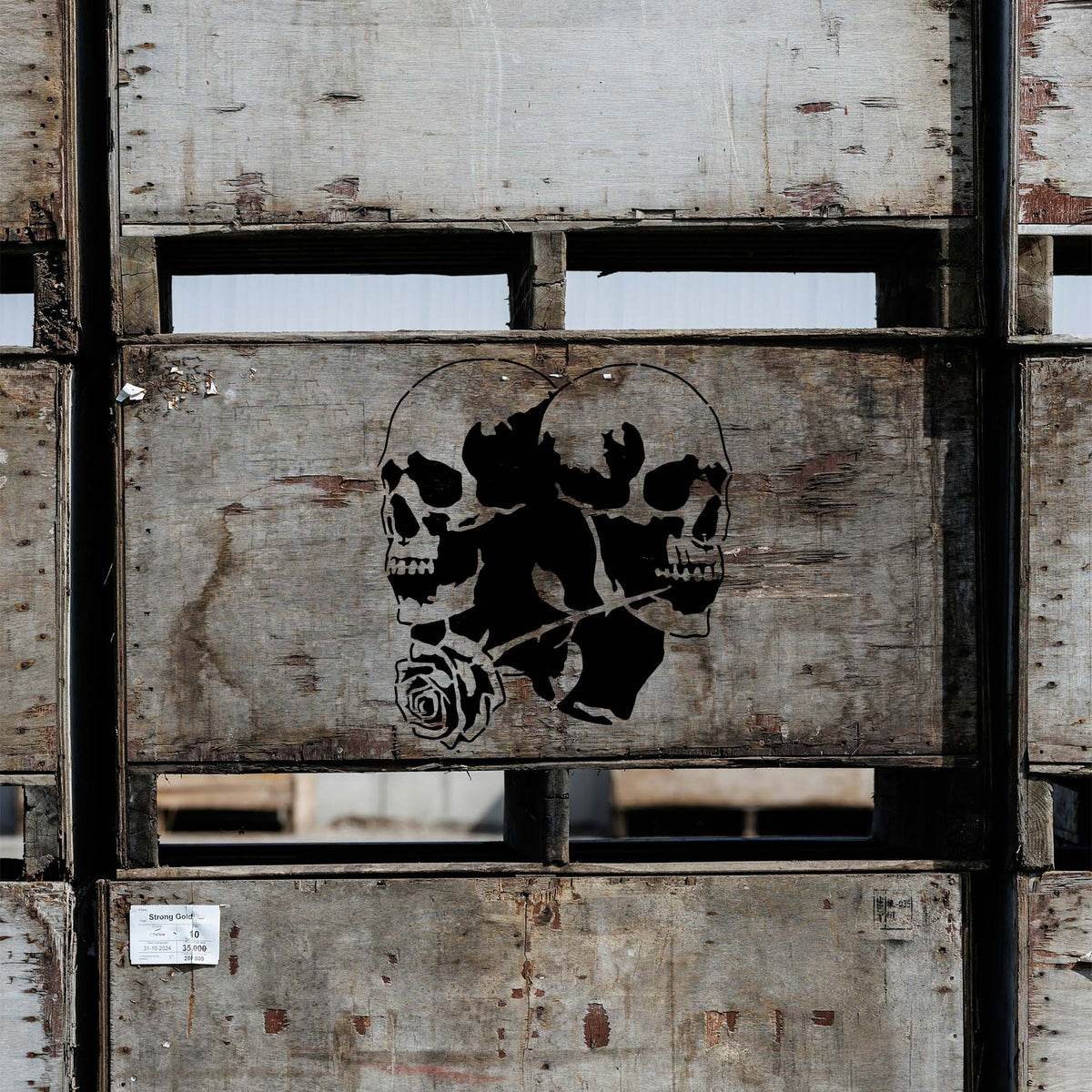 Weathered wooden crates showcase the Twin Skull Rose Stencil with two skulls and a sweeping rose