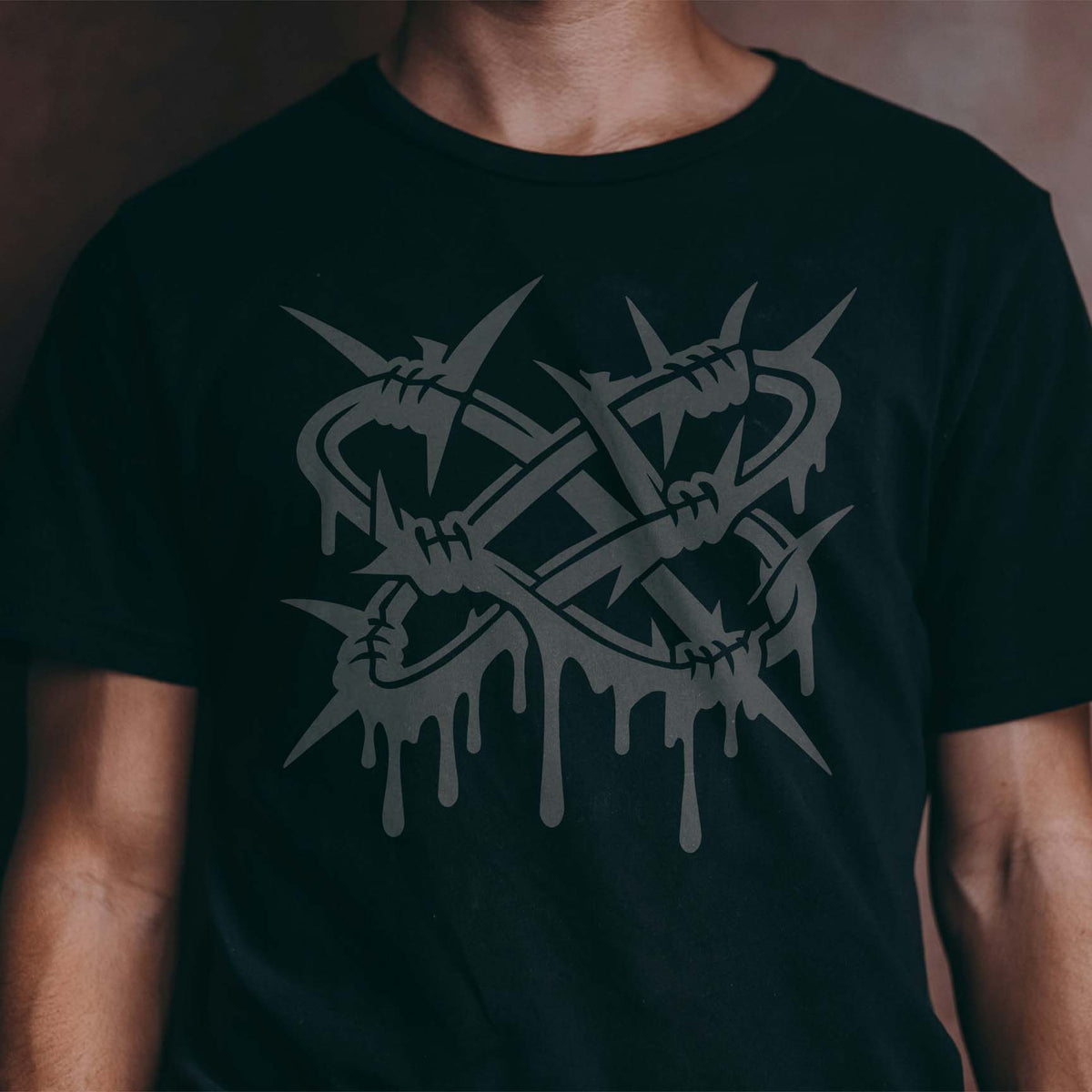 A dark gray Twisted Barbed Wire Stencil features tangled sharp spikes and dripping graffiti on a black t-shirt.