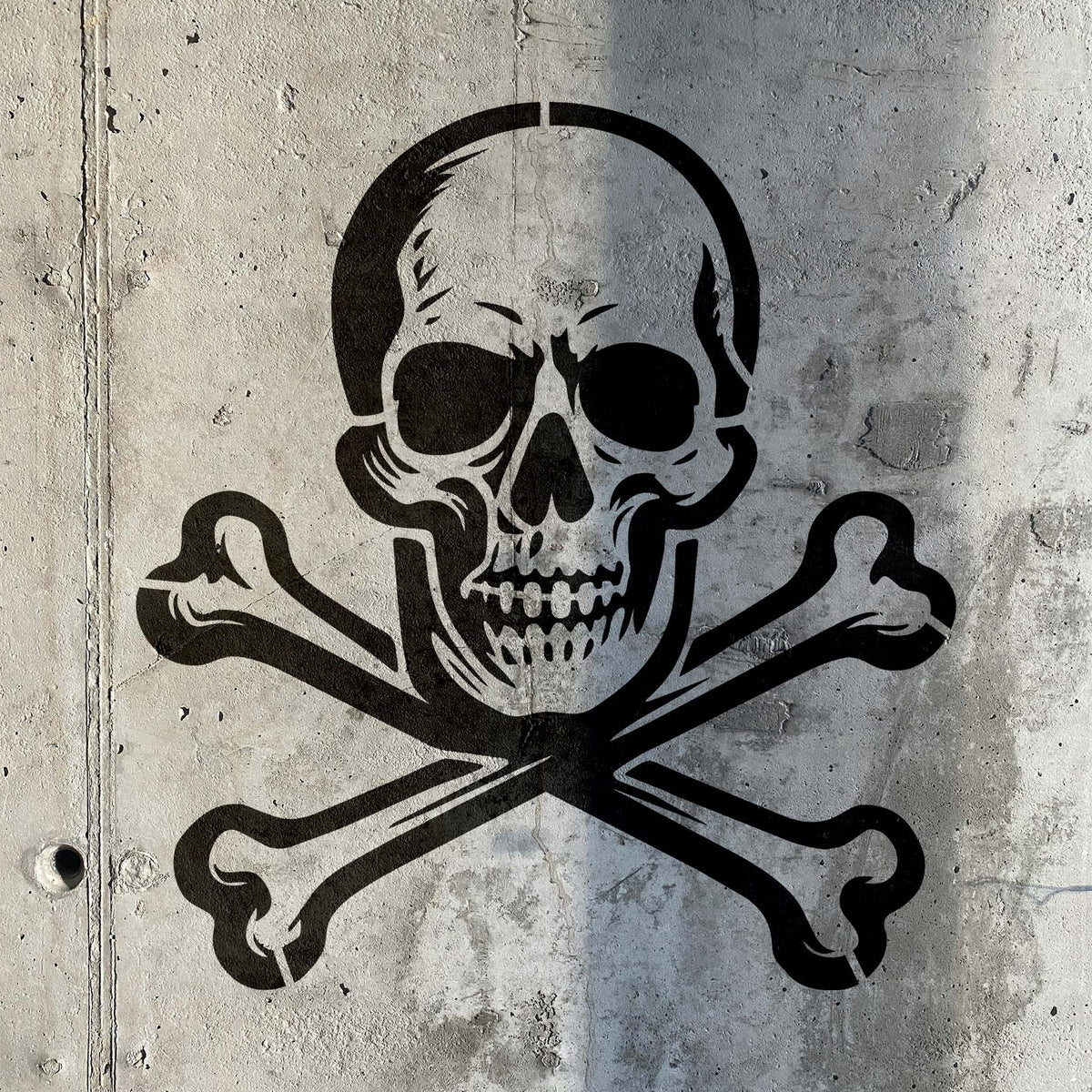 Vintage Skull and Crossbones Stencil painted in black across a rough industrial concrete wall