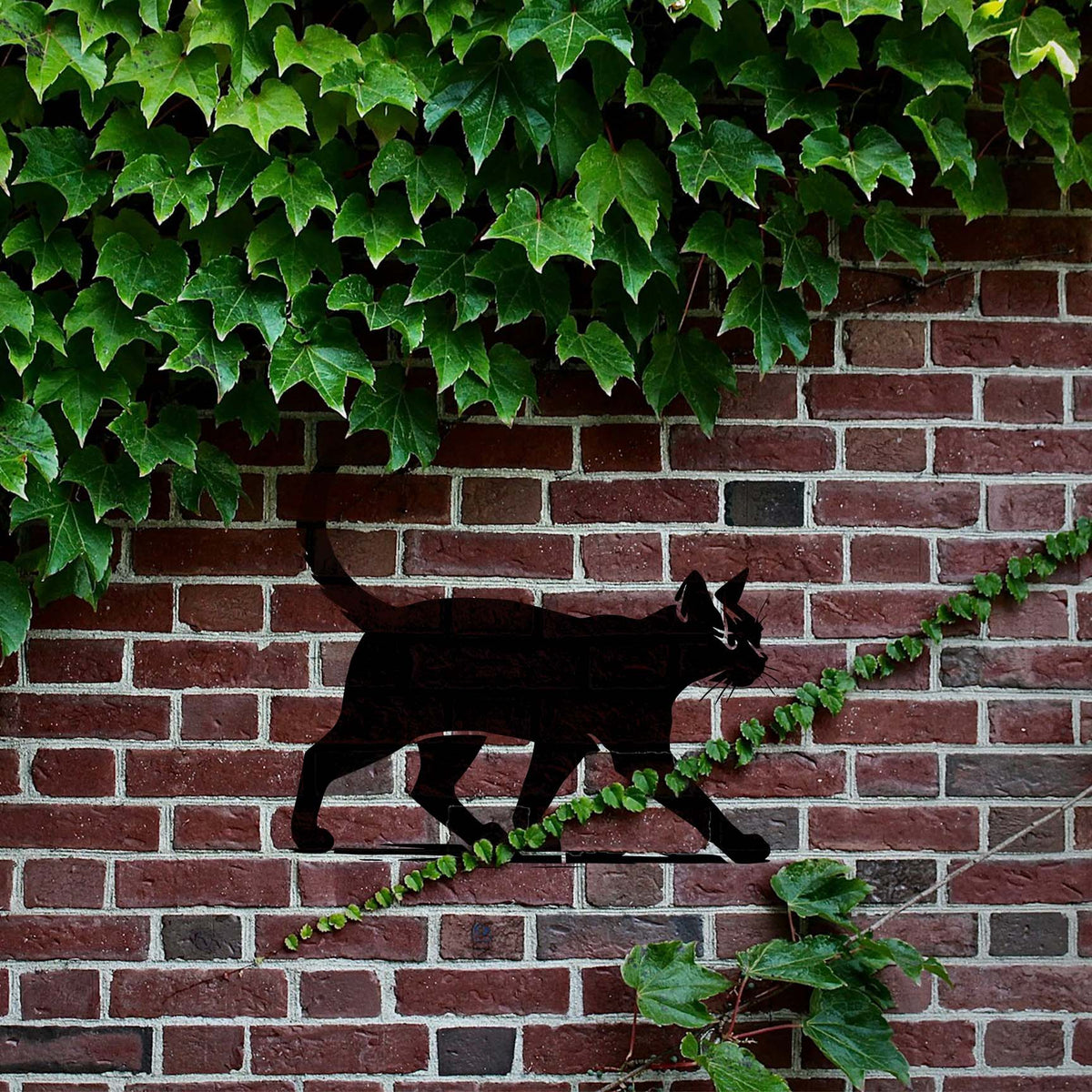 Walking Cat Silhouette Stencil prowls across a brick wall framed by lush green ivy