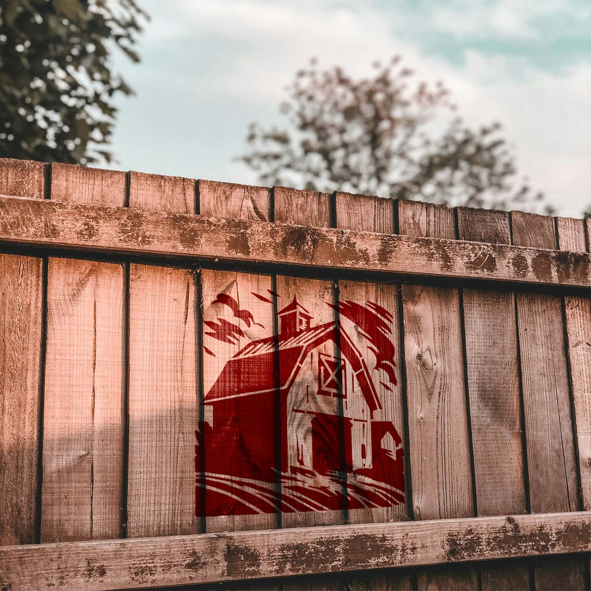 Weathered Farm Barn Stencil painted in dark red on a weathered wooden fence outdoors.