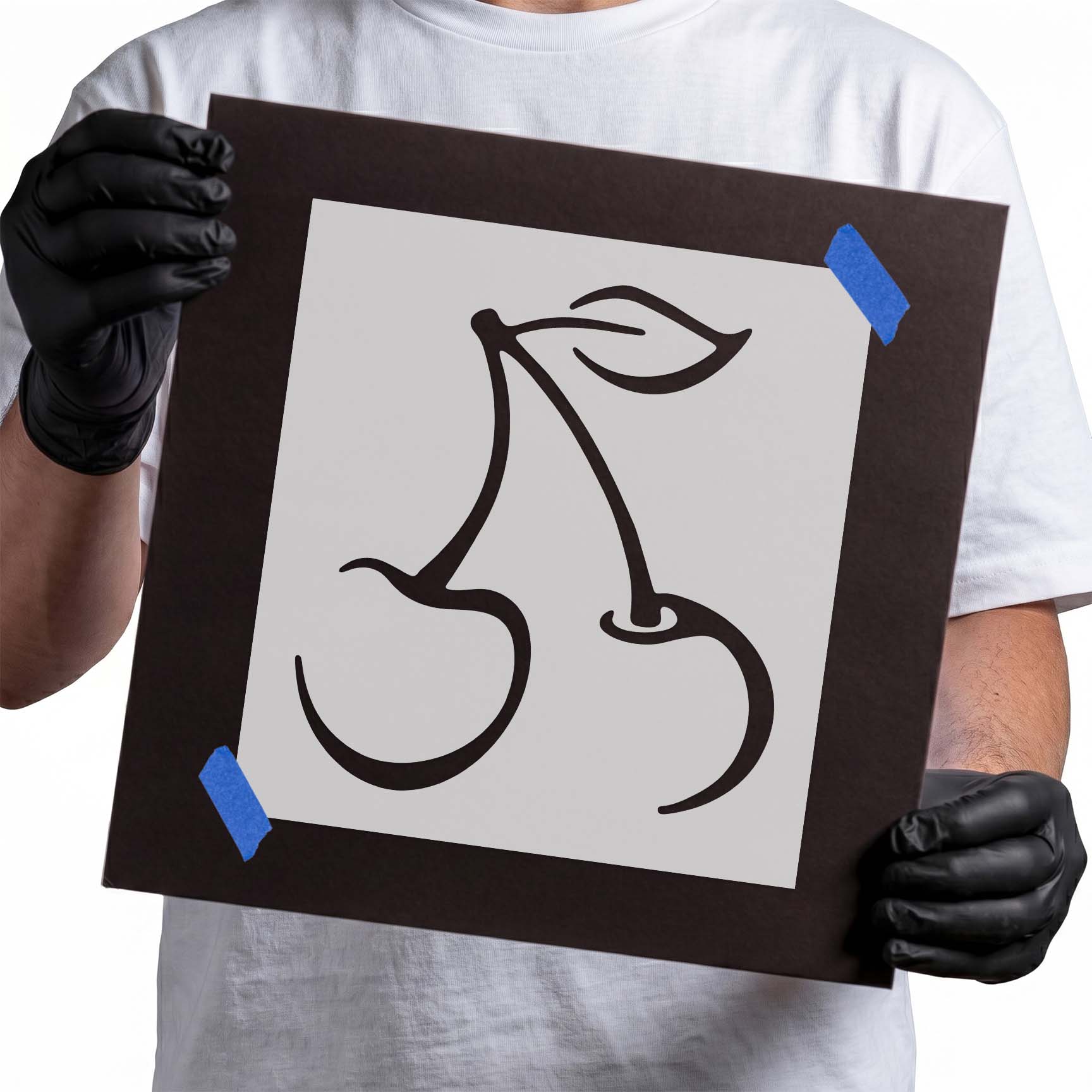 Person holding reusable cherry stencil with two cherries and leaf.