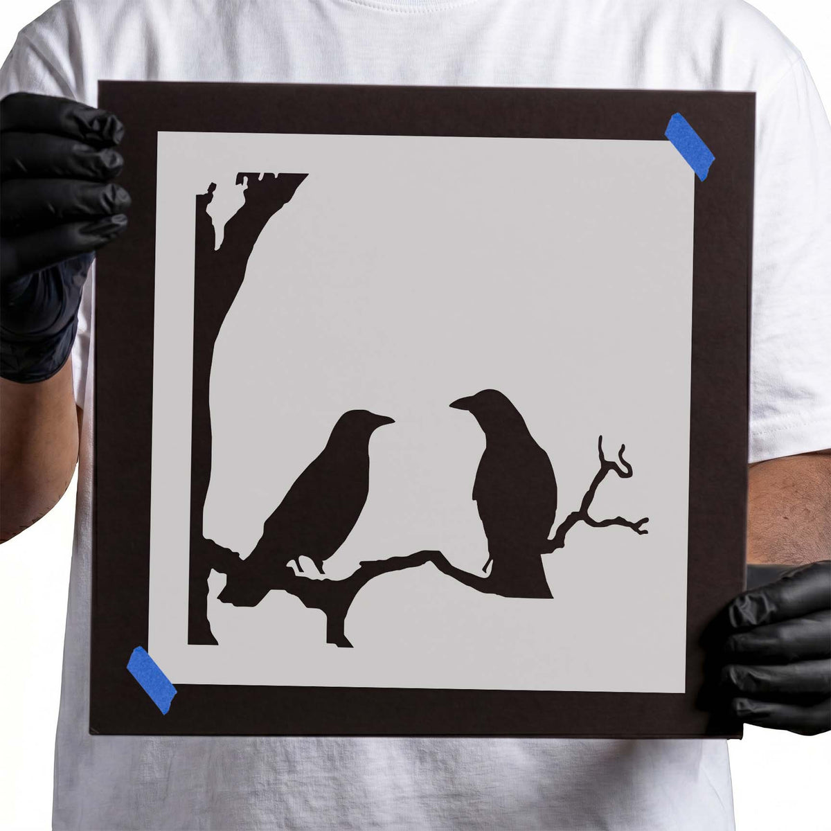 Two crow stencil silhouettes perched facing each other on a branch
