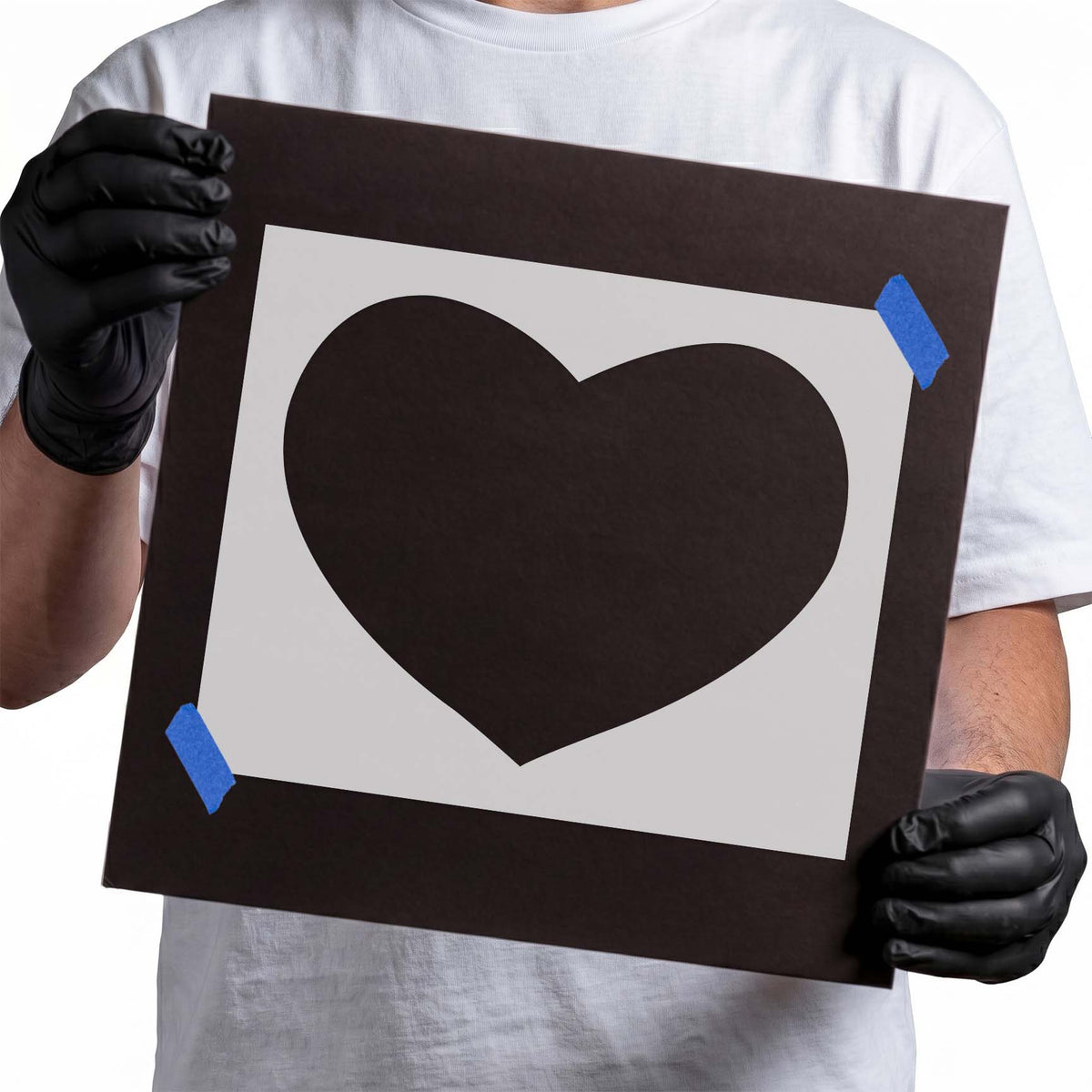 Gloved hands holding laser-cut Heart Stencil taped to cardboard