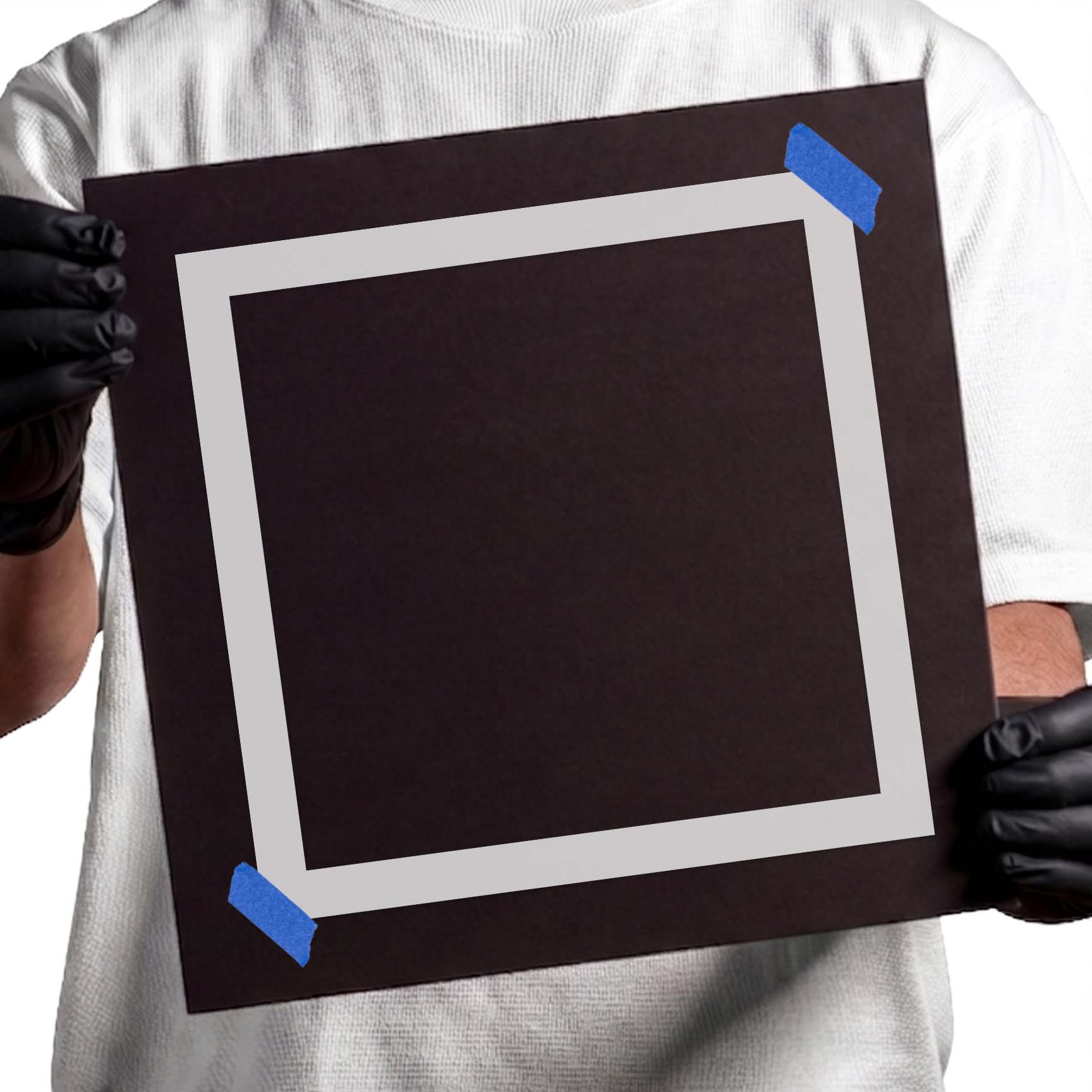 Gloved hands holding Mylar Square Stencil taped to cardboard
